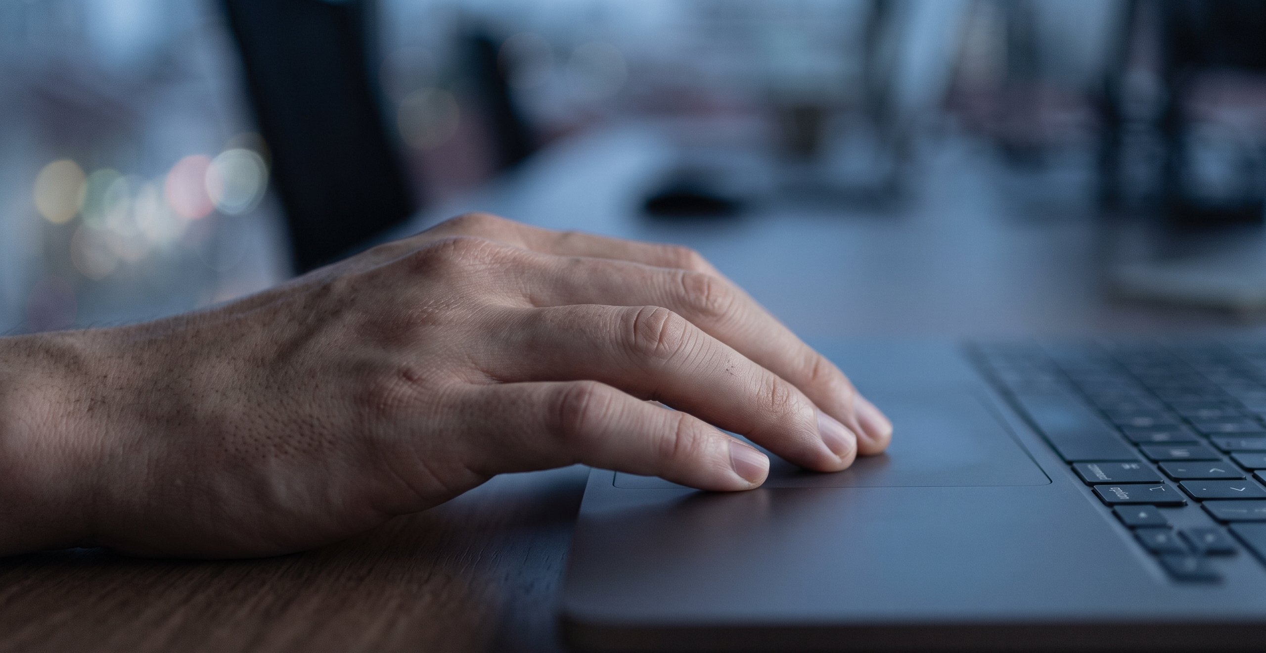 A hand resting on a laptop trackpad, paused before clicking