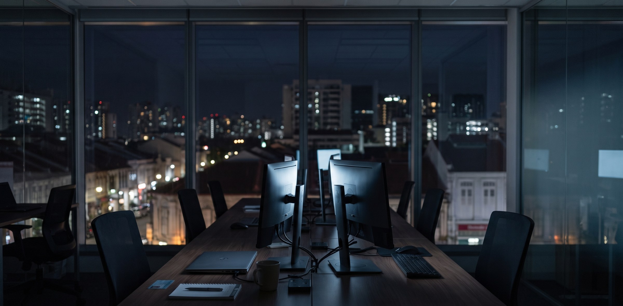 An empty Singapore office at night, monitors still on